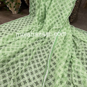 May include: A light green sheer fabric with a white embroidered floral pattern. The fabric has a white lace trim along the edge.