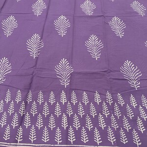 May include: Purple fabric with a white leaf pattern. The fabric has a border with a white geometric pattern.
