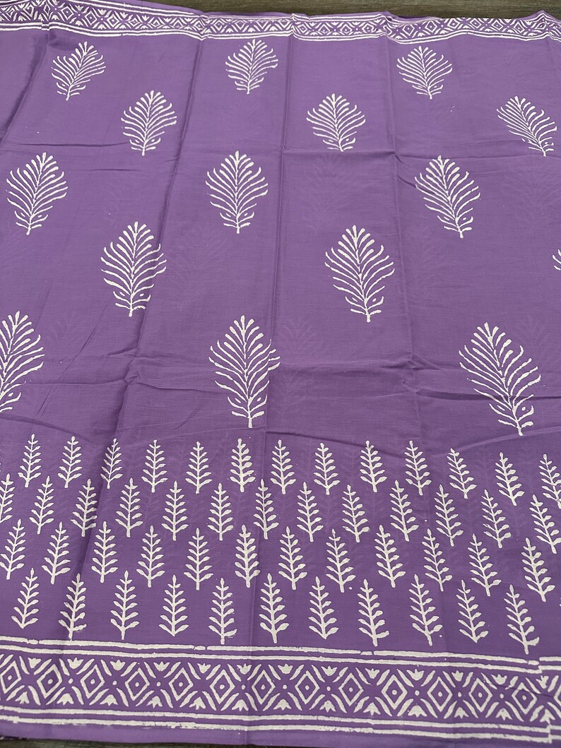 May include: Purple fabric with a white leaf pattern. The fabric has a border with a white geometric pattern.