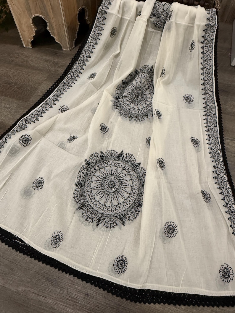 Pode incluir: Tecido branco com desenhos de mandala pretos e detalhes florais. As bordas s&atilde;o adornadas com uma borda de renda preta. O tecido &eacute; drapeado, mostrando os padr&otilde;es e texturas intrincados.