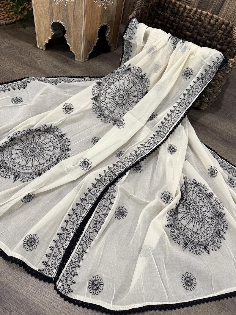 Pode incluir: Len&ccedil;o creme com intrincados padr&otilde;es de mandala pretos e detalhes florais. O len&ccedil;o apresenta uma borda de renda preta. O tecido &eacute; drapeado sobre uma superf&iacute;cie de madeira escura.