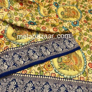 May include: A cream-colored fabric with a blue border and a floral pattern. The fabric features a repeating design of peacocks and flowers in shades of green, yellow, blue, and red. The fabric is called "melabazaar.com".