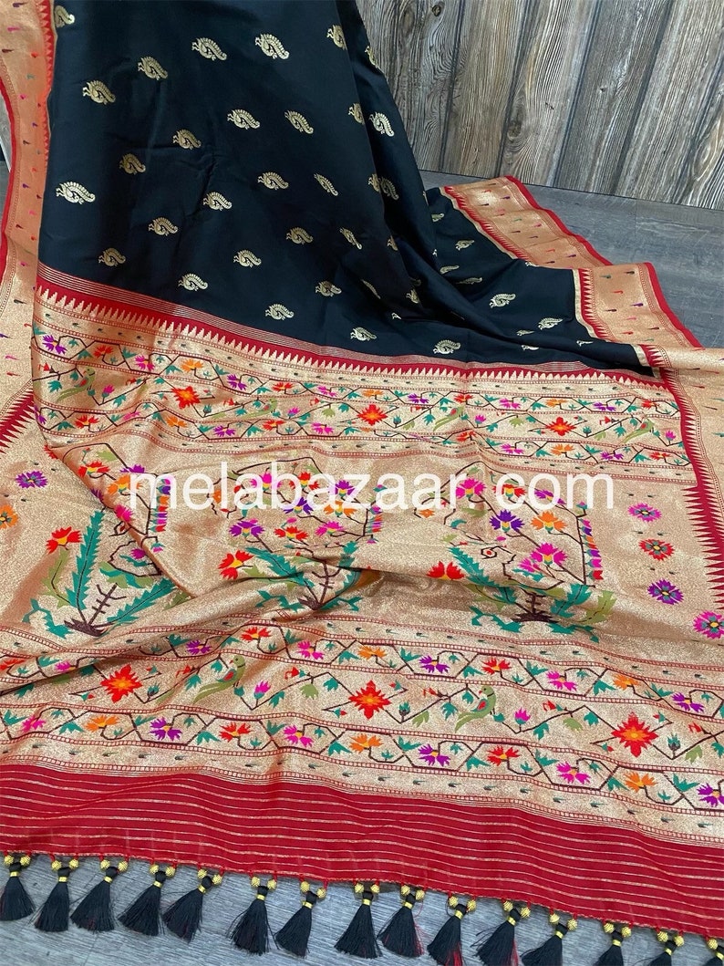 May include: A black and gold saree with a floral pattern and a red border. The saree has a gold and black pallu with a paisley design. The saree has a black tassel trim.