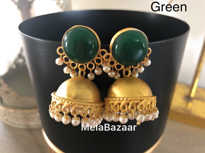 May include: Gold-toned earrings with a green, circular top and a bell-shaped bottom. Small white pearls dangle from the bottom of the earrings. The earrings are displayed in front of a black background. The word "Green" is in the top right corner.