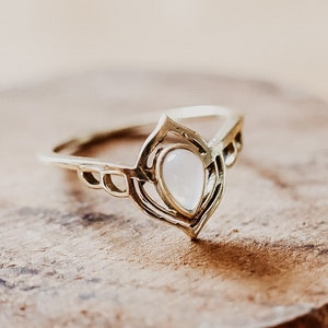 Puede incluir: Un anillo de oro con un diseño delicado e intrincado que presenta una piedra preciosa blanca en forma de pera.