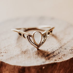 Puede incluir: Un anillo de oro con un delicado diseño en forma de V y una piedra blanca en forma de pera.