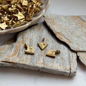 May include: Three gold-toned arrow-shaped pendants with a geometric design. The pendants have a loop at the top for attaching to a chain or cord.