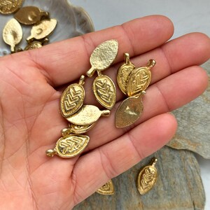 May include: A collection of gold-toned metal leaf charms with a textured surface and a geometric design. The charms have a hole at the top for attaching to jewelry or other crafts.