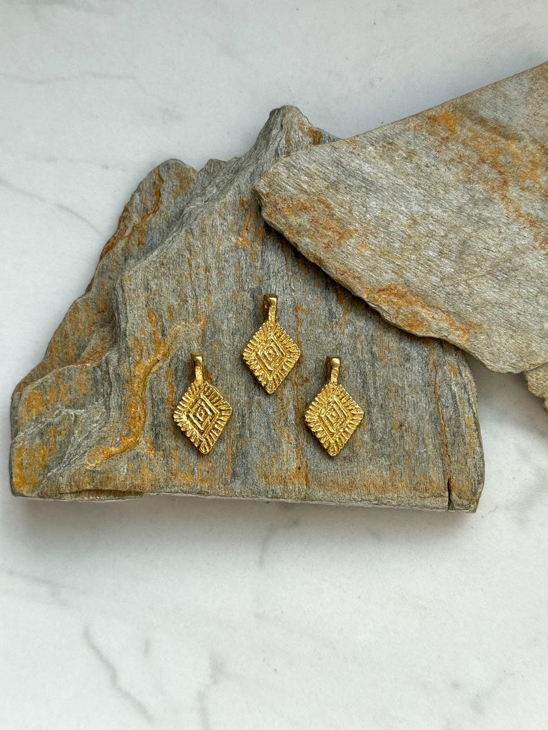 Puede incluir: Tres abalorios de metal de color dorado con un dise&ntilde;o geom&eacute;trico. Los abalorios tienen forma de diamante y una superficie texturizada.
