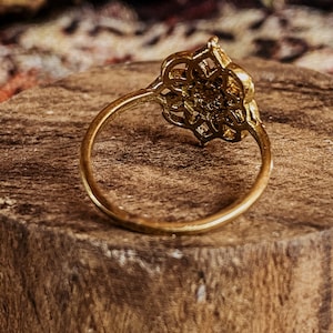 K&ouml;nnte beinhalten: Ein goldener Ring mit einem filigranen, komplizierten Design. Der Ring liegt auf einer Holzoberfl&auml;che.