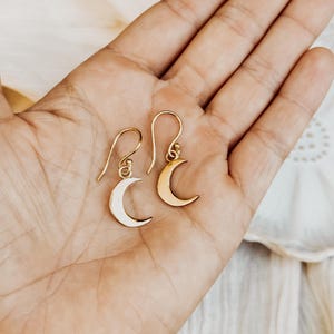 May include: A pair of gold crescent moon earrings. The earrings are delicate and simple, with a minimalist design.