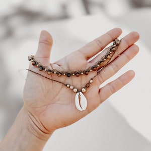 May include: A brown and gold beaded necklace with a white seashell pendant.