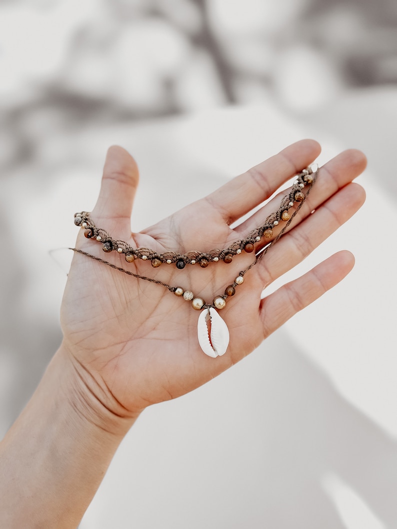 May include: A brown and gold beaded necklace with a white seashell pendant.