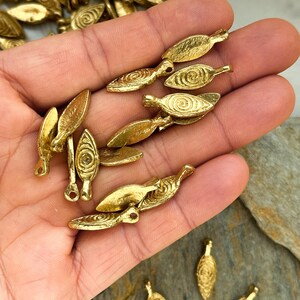 May include: A collection of gold-toned metal leaf-shaped charms with a spiral design. The charms have a hole at the top for attaching to jewelry or other crafts.