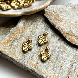 May include: Three gold-colored metal charms with a swirl design. The charms are on a light brown surface.