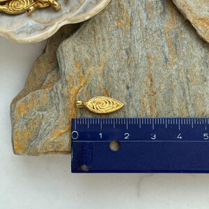 May include: Gold leaf charm with a swirl design, measuring approximately 1 inch in length. The charm is shown next to a ruler for size reference.