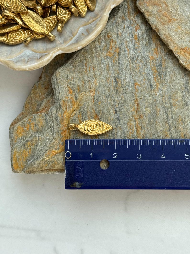 May include: Gold leaf charm with a swirl design, measuring approximately 1 inch in length. The charm is shown next to a ruler for size reference.