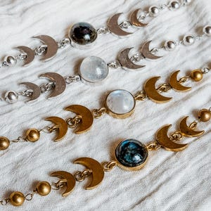 May include: Four bracelets featuring a series of metal crescent moon charms and round beads. Two bracelets are silver-toned with clear and dark stones, while two are gold-toned with iridescent and dark blue stones set in circular bezels.