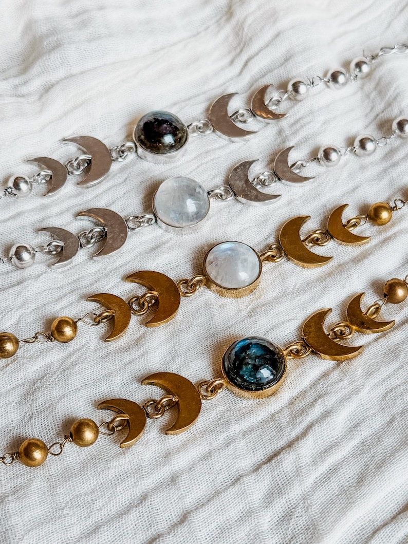 May include: Four bracelets featuring a series of metal crescent moon charms and round beads. Two bracelets are silver-toned with clear and dark stones, while two are gold-toned with iridescent and dark blue stones set in circular bezels.