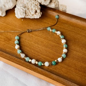 Puede incluir: Una pulsera de cuentas que alterna cuentas redondas de color verde menta, cuentas blancas lisas y peque&ntilde;os espaciadores met&aacute;licos facetados en tono dorado. La pulsera est&aacute; hecha con un cord&oacute;n marr&oacute;n fino y un cierre de nudo corredizo.