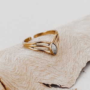 Könnte beinhalten: Ein goldener Ring mit einem klaren Edelstein, der in einem V-förmigen Design gefasst ist.