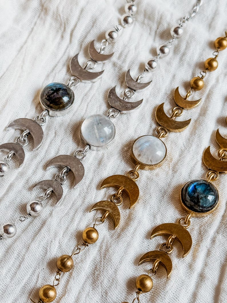 May include: Four necklaces featuring a series of crescent moon charms and round beads. Two necklaces are silver-toned with dark and clear round stones, while two are gold-toned with dark and clear round stones, all arranged in a repeating pattern.