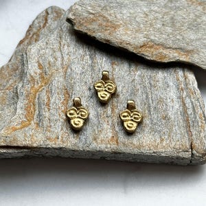 May include: Three gold-colored metal charms with a clover design. The charms are on a piece of rough, gray rock.
