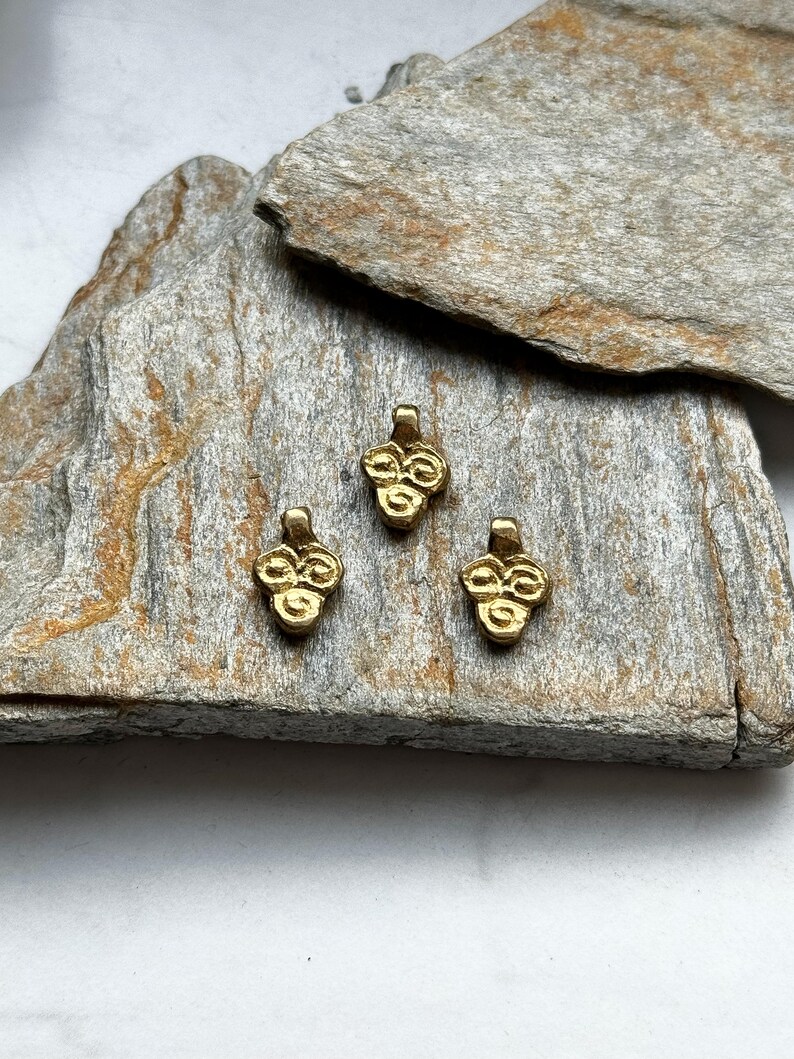 May include: Three gold-colored metal charms with a clover design. The charms are on a piece of rough, gray rock.