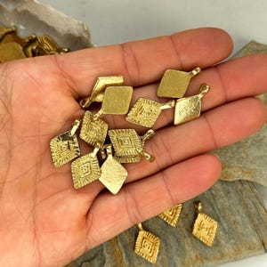Puede incluir: Una colecci&oacute;n de dijes de metal dorado en forma de diamante con intrincados dise&ntilde;os geom&eacute;tricos. Cada dije tiene un peque&ntilde;o bucle en la parte superior para sujetarlo a joyas u otras manualidades.