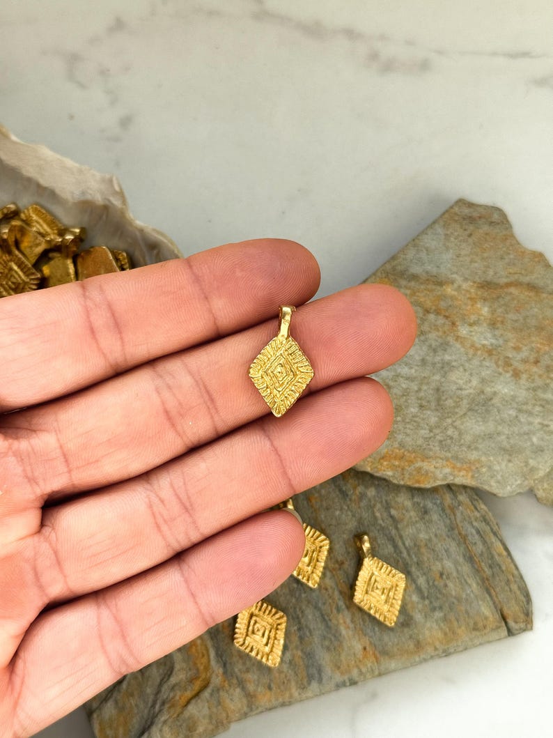 Puede incluir: Encantos de colgante de metal dorado con forma de diamante geom&eacute;trico y detalles intrincados. Los encantos tienen un bucle en la parte superior para sujetar a las joyas.