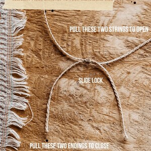 May include: A beige braided cord jewelry slide lock mechanism featuring text instructions: WITH THIS SLIDE LOCK YOU CAN ADJUST YOUR JEWELRY PIECE EXACTLY TO YOUR INDIVIDUAL SIZE, PULL THESE TWO STRINGS TO OPEN, SLIDE LOCK, PULL THESE TWO ENDINGS TO CLOSE.