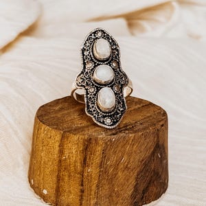 Puede incluir: Un anillo de plata con un diseño adornado y tres piedras de luna blanca.