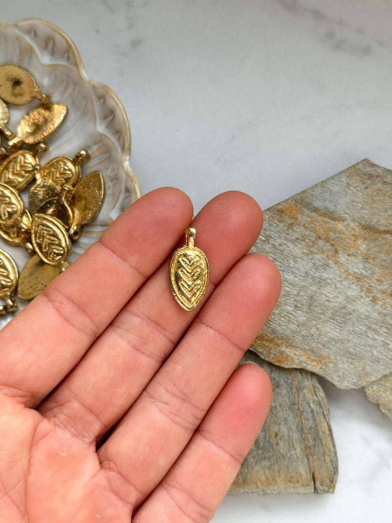 May include: A gold leaf charm with a detailed geometric pattern. The charm is small and delicate, perfect for adding a touch of elegance to jewelry.