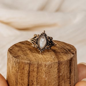Puede incluir: Un anillo de oro con una piedra de luna blanca engastada en un diseño detallado y ornamentado.