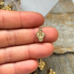 May include: Gold-toned metal pendant with a decorative design of four circles. The pendant has a loop at the top for attaching to a chain or cord.