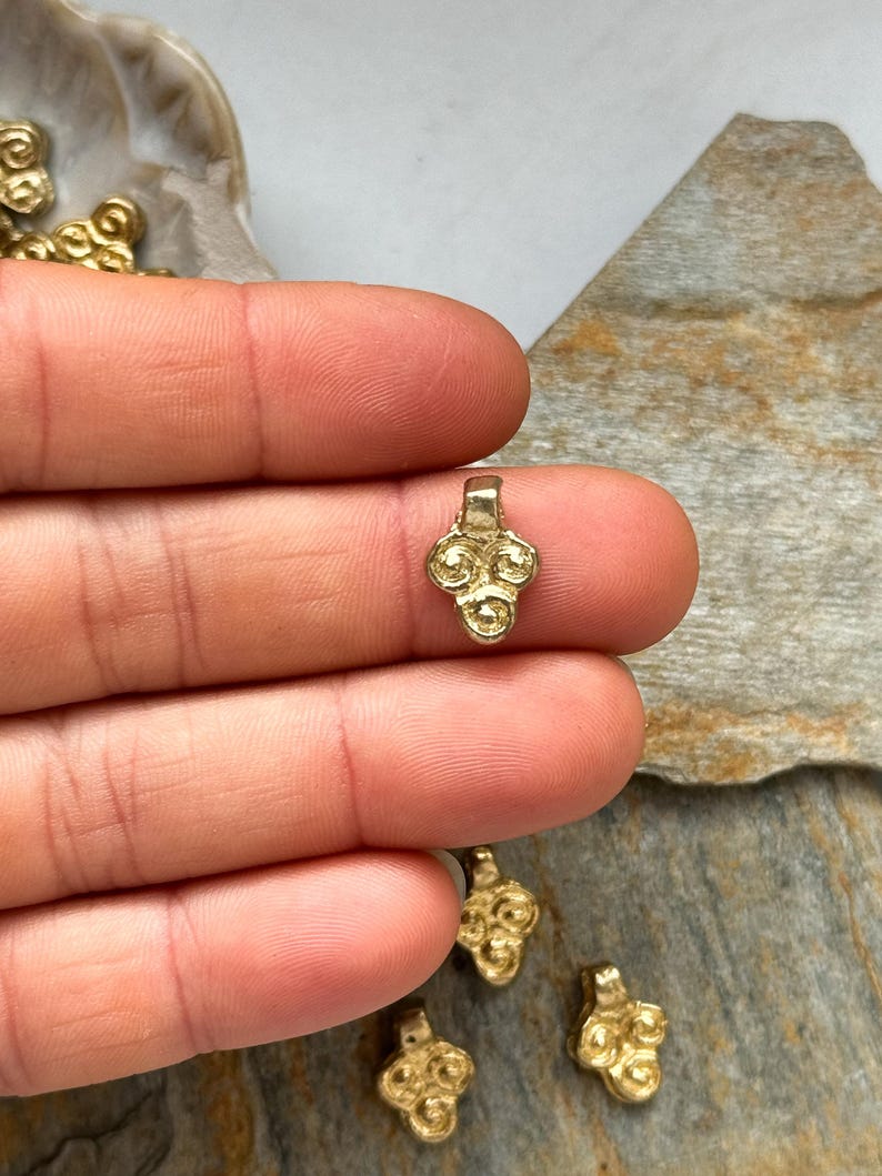 May include: Gold-toned metal pendant with a decorative design of four circles. The pendant has a loop at the top for attaching to a chain or cord.
