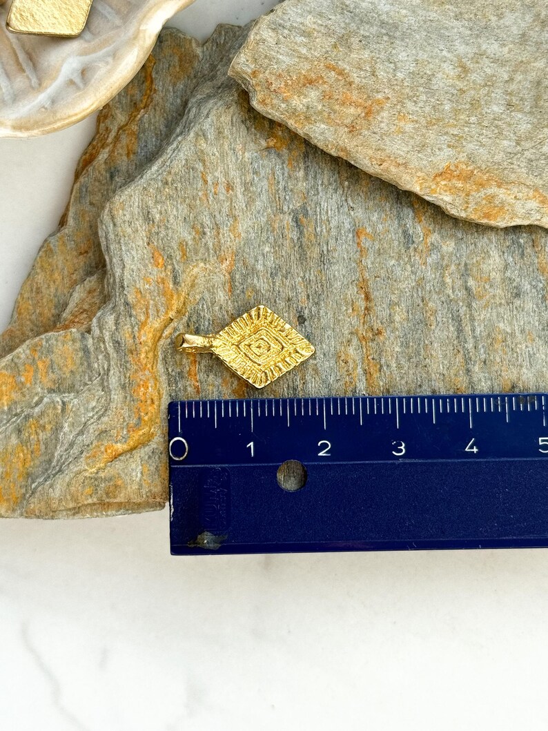 Puede incluir: Un colgante de color dorado en forma de diamante con un dise&ntilde;o intrincado. El colgante mide aproximadamente 2,5 cm de largo.