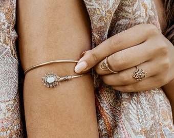 Puede incluir: Un brazalete de oro para el brazo con una piedra blanca decorativa y un diseño delicado. El brazalete se lleva en la parte superior del brazo.
