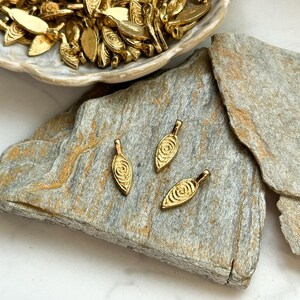 May include: Three gold leaf-shaped charms with a swirl design. The charms have a hole at the top for attaching to jewelry or other crafts.