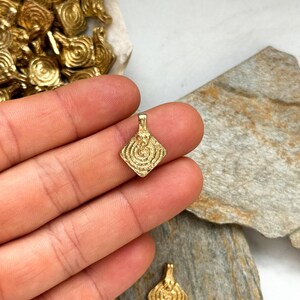 K&ouml;nnte beinhalten: Goldfarbener Metallanh&auml;nger mit quadratischer Form und einem wirbelnden, konzentrischen Kreisdesign. Der Anh&auml;nger hat eine &Ouml;se oben zum Anbringen an einer Kette oder Schnur.
