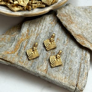 K&ouml;nnte beinhalten: Drei goldfarbene Metallanh&auml;nger in quadratischer Form mit einem wirbelnden Design. Die Anh&auml;nger haben eine &Ouml;se oben zum Anbringen an einer Kette oder Schnur.