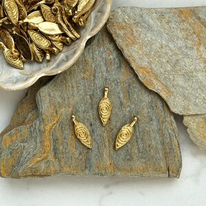 May include: Three gold-colored metal pendants with a swirl design. The pendants are on a gray stone surface.