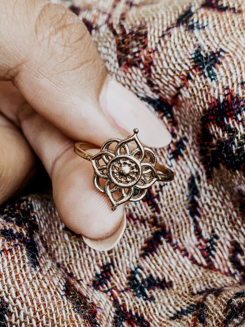 K&ouml;nnte beinhalten: Ein goldfarbener Ring mit einem filigranen, komplizierten Design, das an eine Blume erinnert. Der Ring wird an einem Finger getragen und zeigt die filigranen Details des Designs.