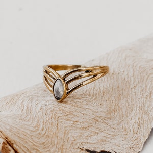 Puede incluir: Un anillo de oro con una piedra clara y facetada engastada en una banda en forma de V. El anillo está hecho de tres bandas entrelazadas.