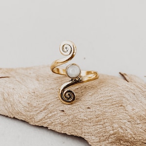 Puede incluir: Un anillo de oro con una piedra blanca y un diseño en espiral.