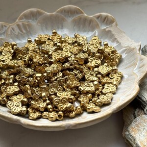 May include: A bowl filled with gold-colored metal beads. Each bead is shaped like a stylized flower with a hole in the center for stringing.