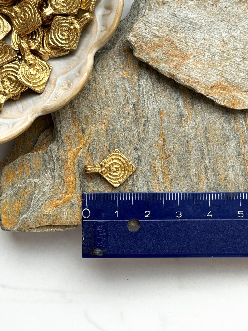 K&ouml;nnte beinhalten: Goldfarbener Metallanh&auml;nger mit Spiraldesign. Der Anh&auml;nger hat die Form eines Diamanten und ist etwa 2,5 cm lang. Der Anh&auml;nger wird neben einem Lineal zur Gr&ouml;&szlig;enreferenz gezeigt.