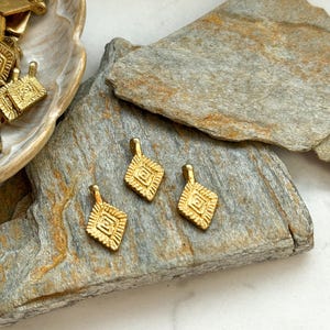 Puede incluir: Tres abalorios de metal dorado con un dise&ntilde;o geom&eacute;trico. Los abalorios tienen forma de diamante y un patr&oacute;n en relieve.