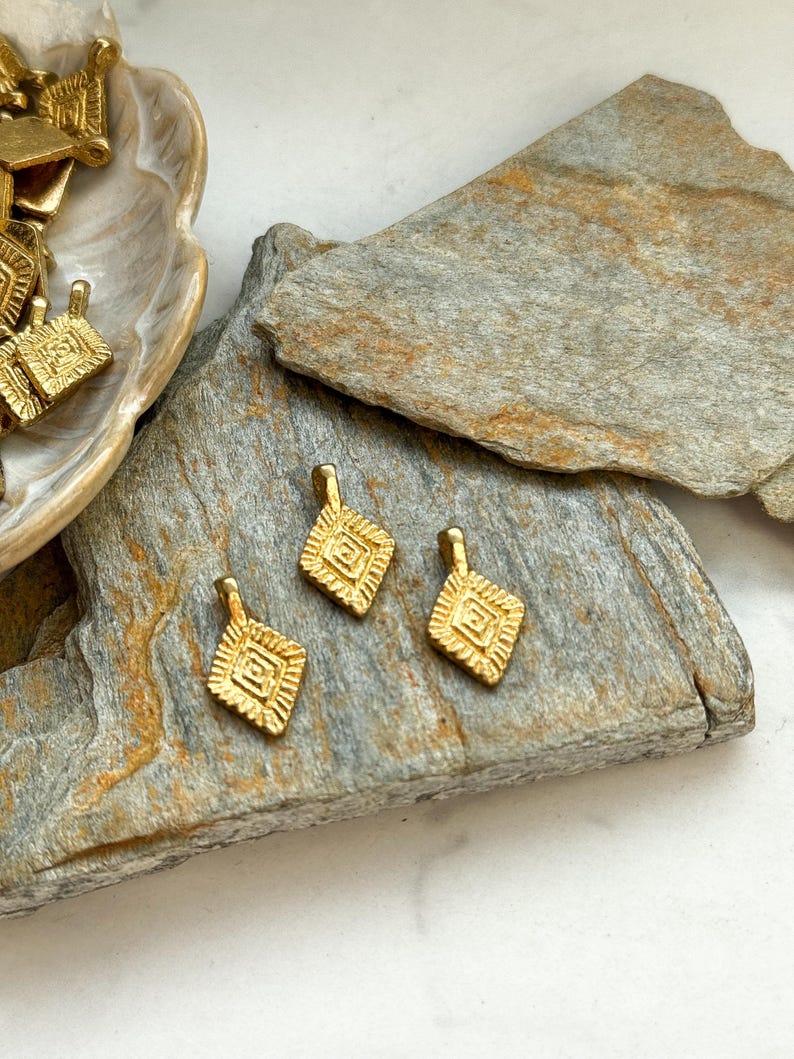 Puede incluir: Tres abalorios de metal dorado con un dise&ntilde;o geom&eacute;trico. Los abalorios tienen forma de diamante y un patr&oacute;n en relieve.