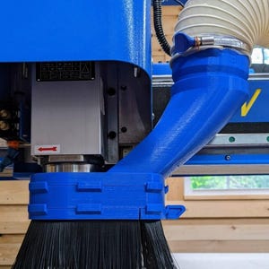 May include: Close-up of a blue dust collection system for a CNC router. The system features a brush to remove debris from the work surface and a hose to connect to a dust collector.